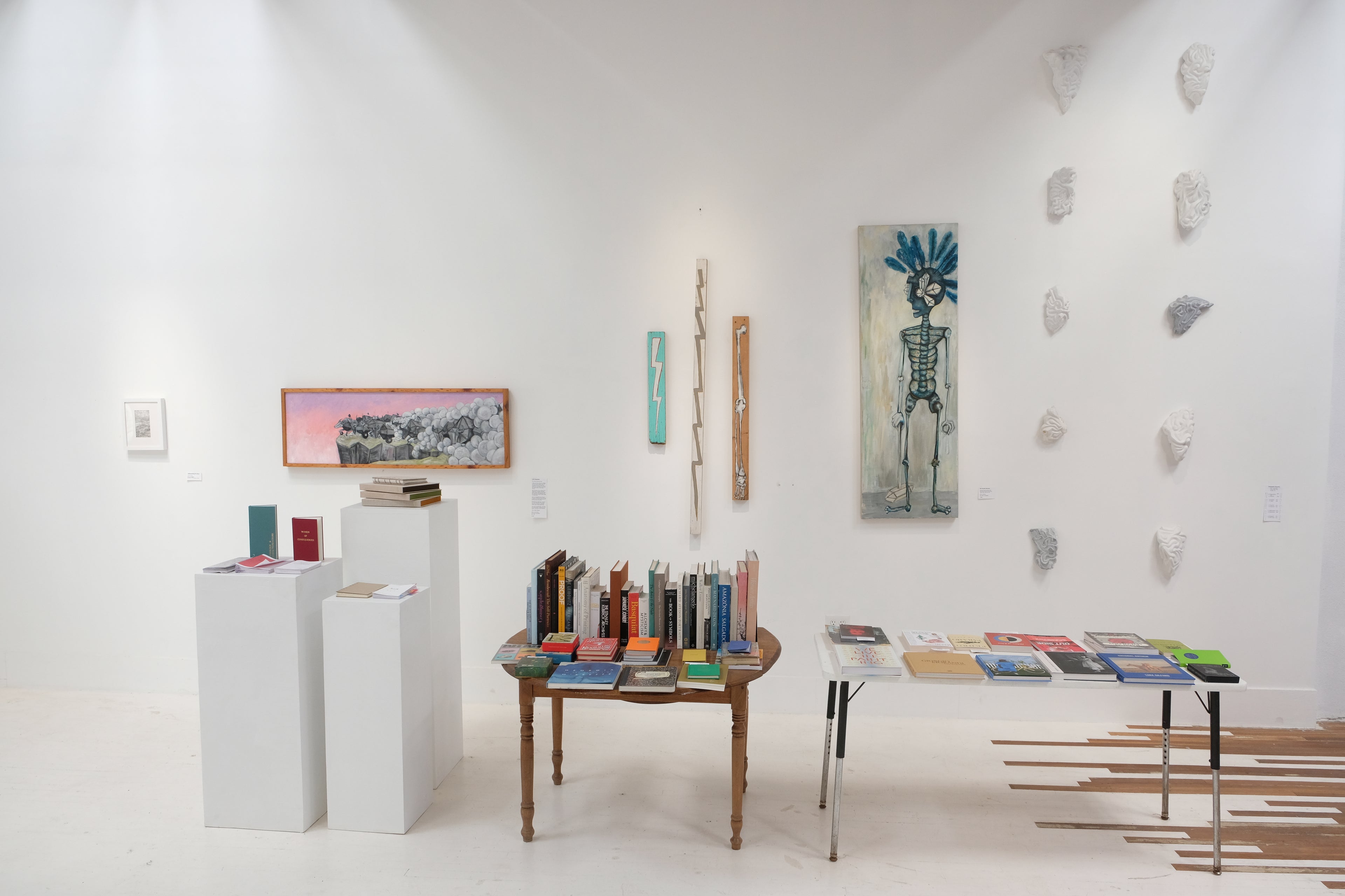 Art gallery with various artworks on the walls and tables displaying books.